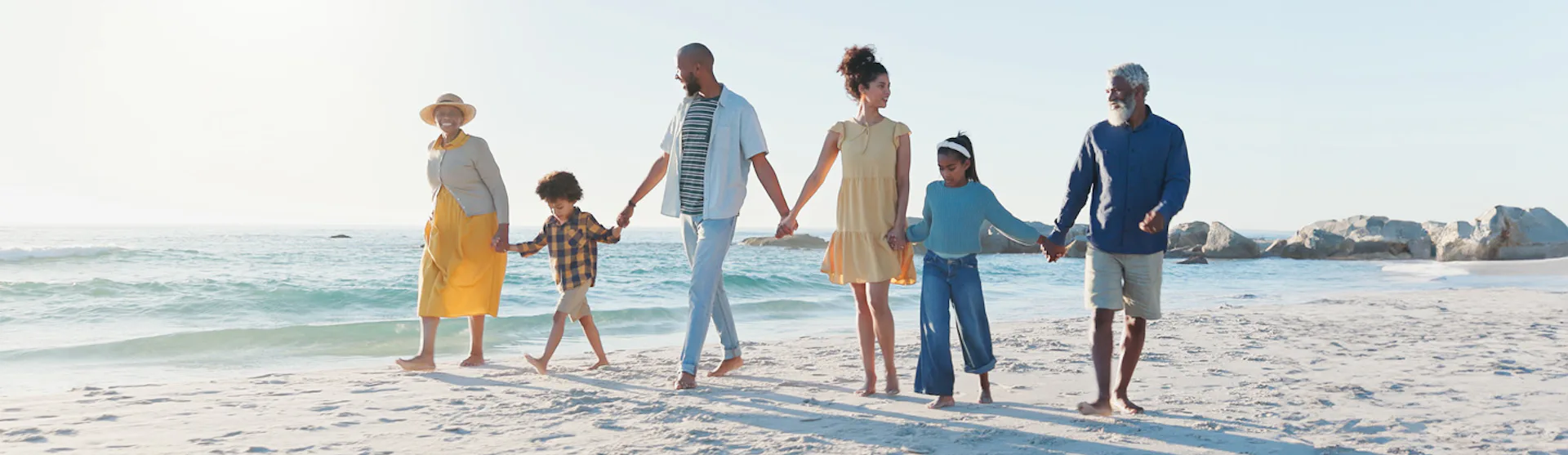 Stor familj håller hand på stranden.
