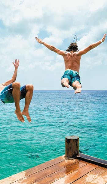 Tre killar hoppar i vattnet från en brygga i Cozumel, Mexiko.