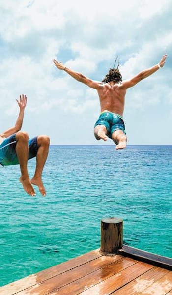 Tre killar hoppar i vattnet från en brygga i Cozumel, Mexiko.