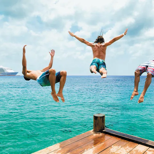 Tre killar hoppar i vattnet från en brygga i Cozumel, Mexiko.