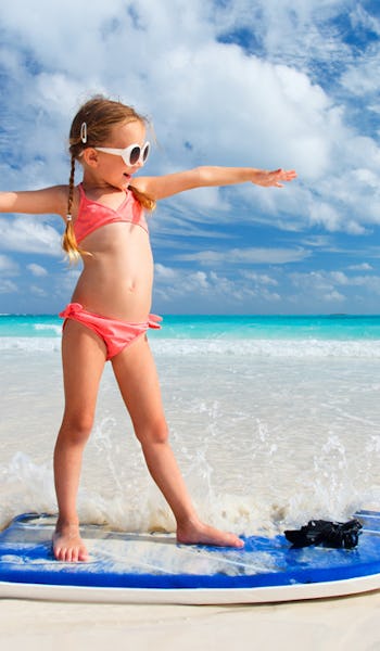 Söt liten tjej på surfbräda i strandkanten.
